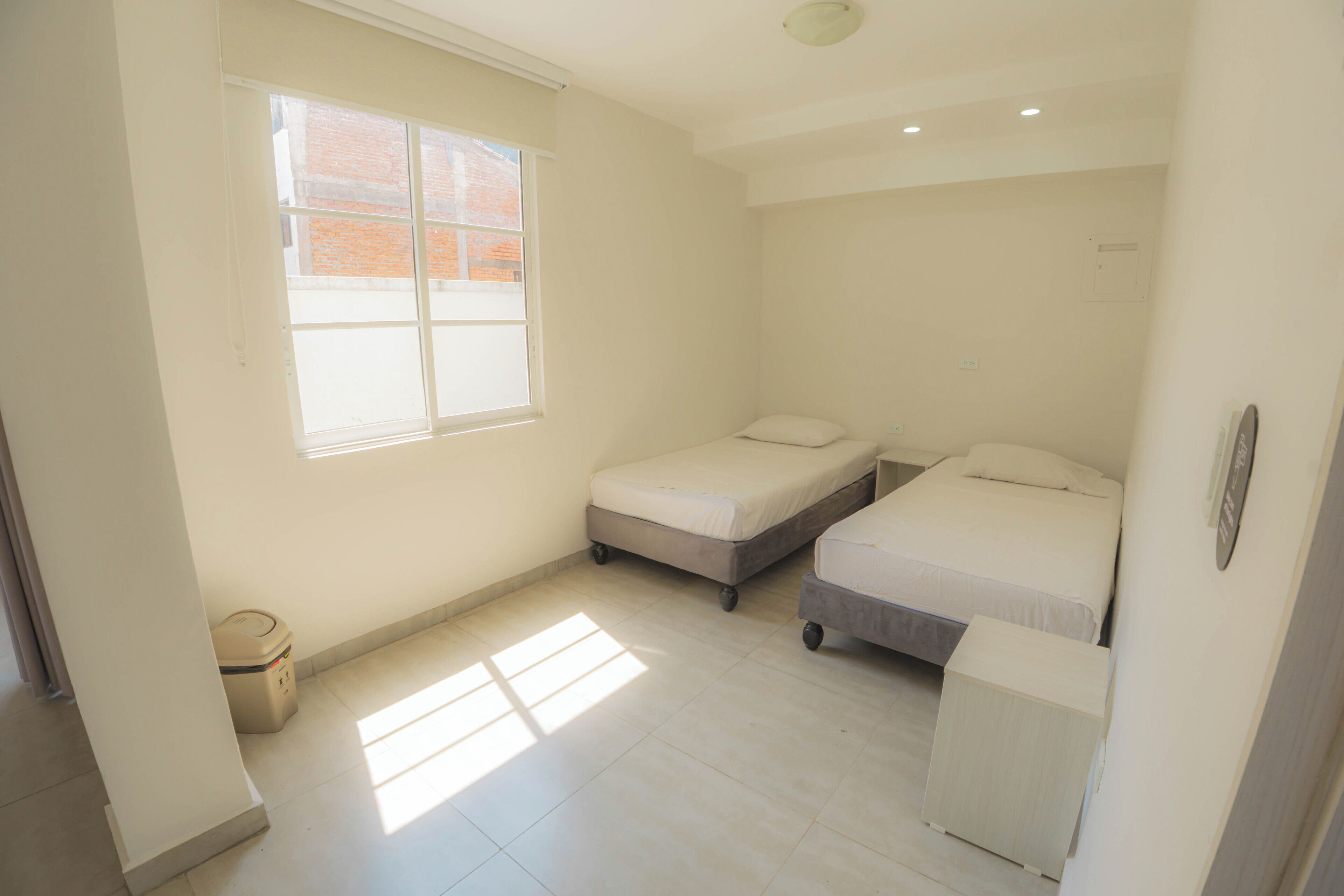A small, well-lit room with two single beds, a small table, and a window.