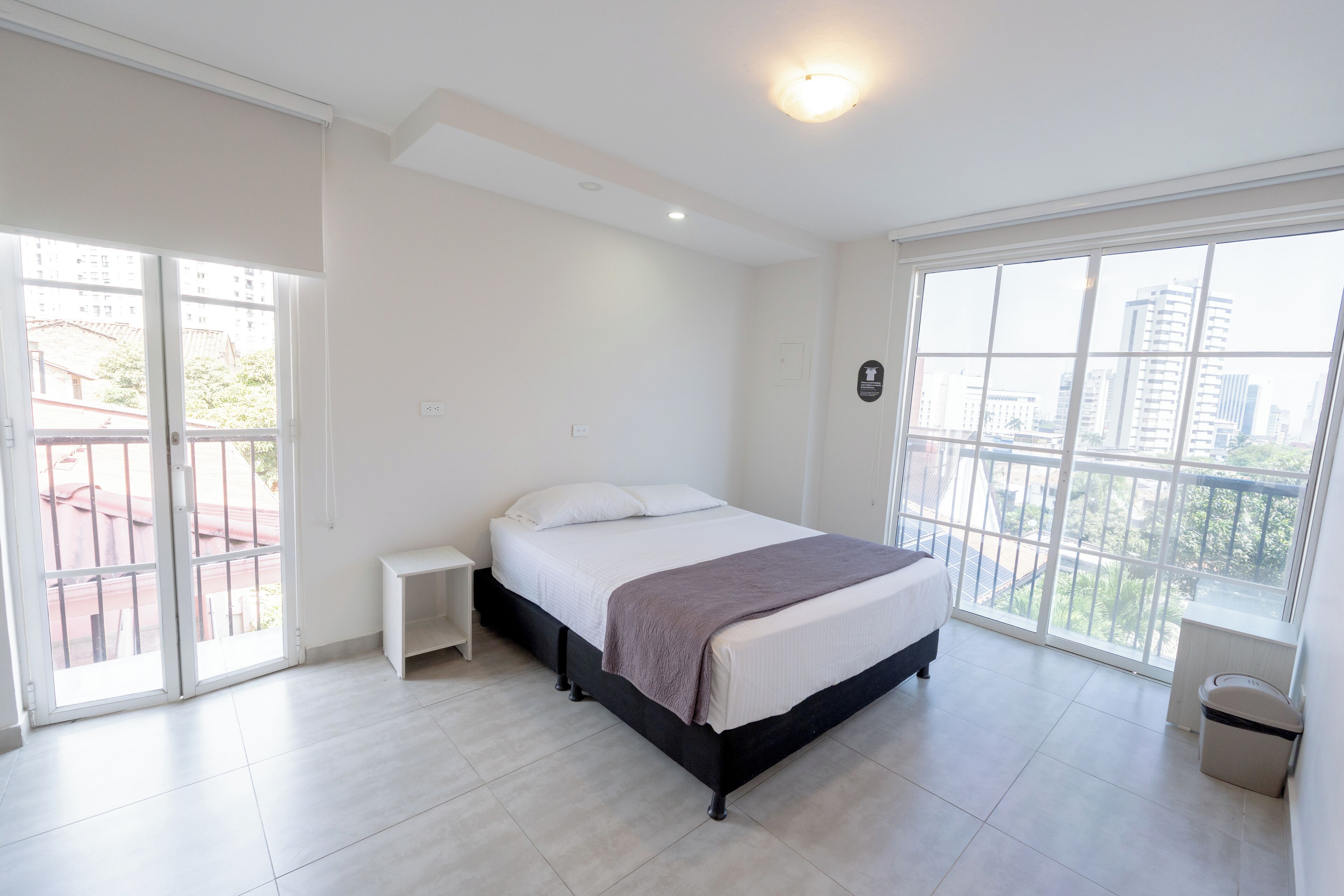 A bedroom with a bed, a nightstand, a window, and a balcony.