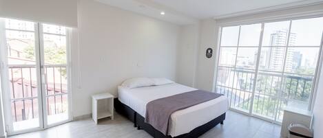 A bedroom with a bed, a nightstand, a window, and a balcony.