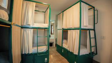 Bunk beds with curtains, a trash bin, and a hallway leading to a bathroom.