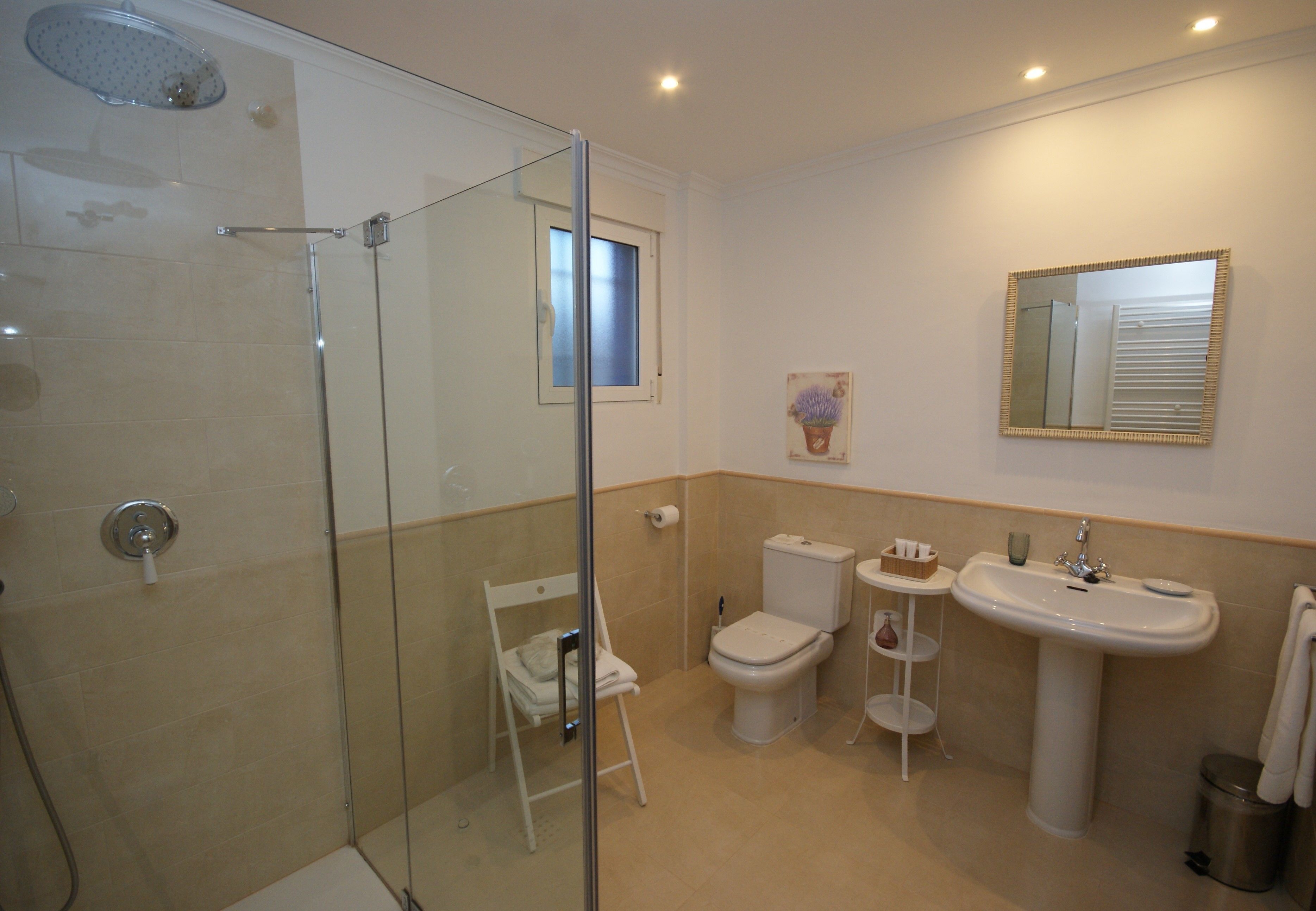 A bathroom with a glass-enclosed shower, a toilet, a sink, and a small window.