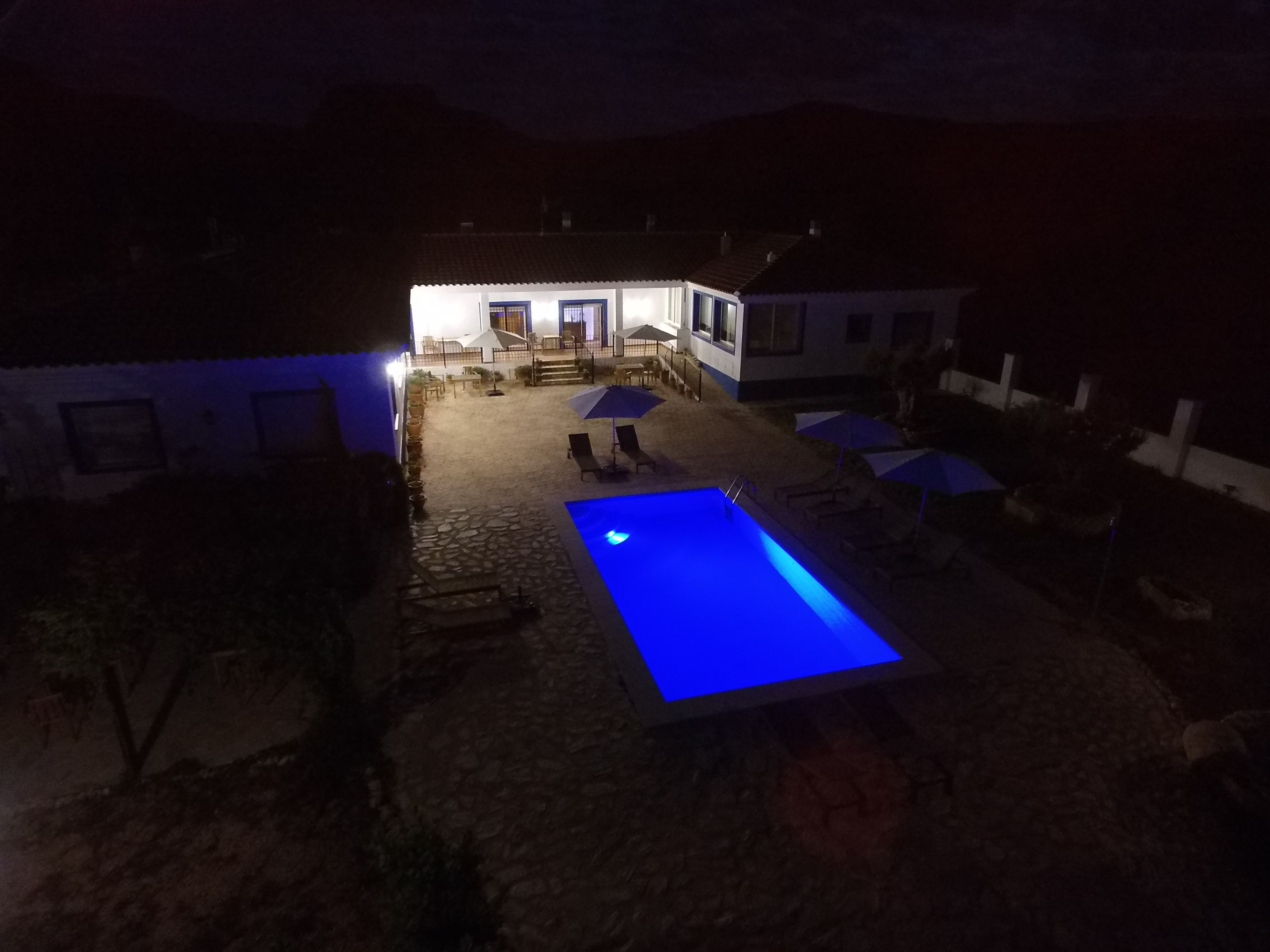 Un espace piscine avec une piscine illuminée de lumière bleue, des sièges extérieurs et un bâtiment en arrière-plan.
