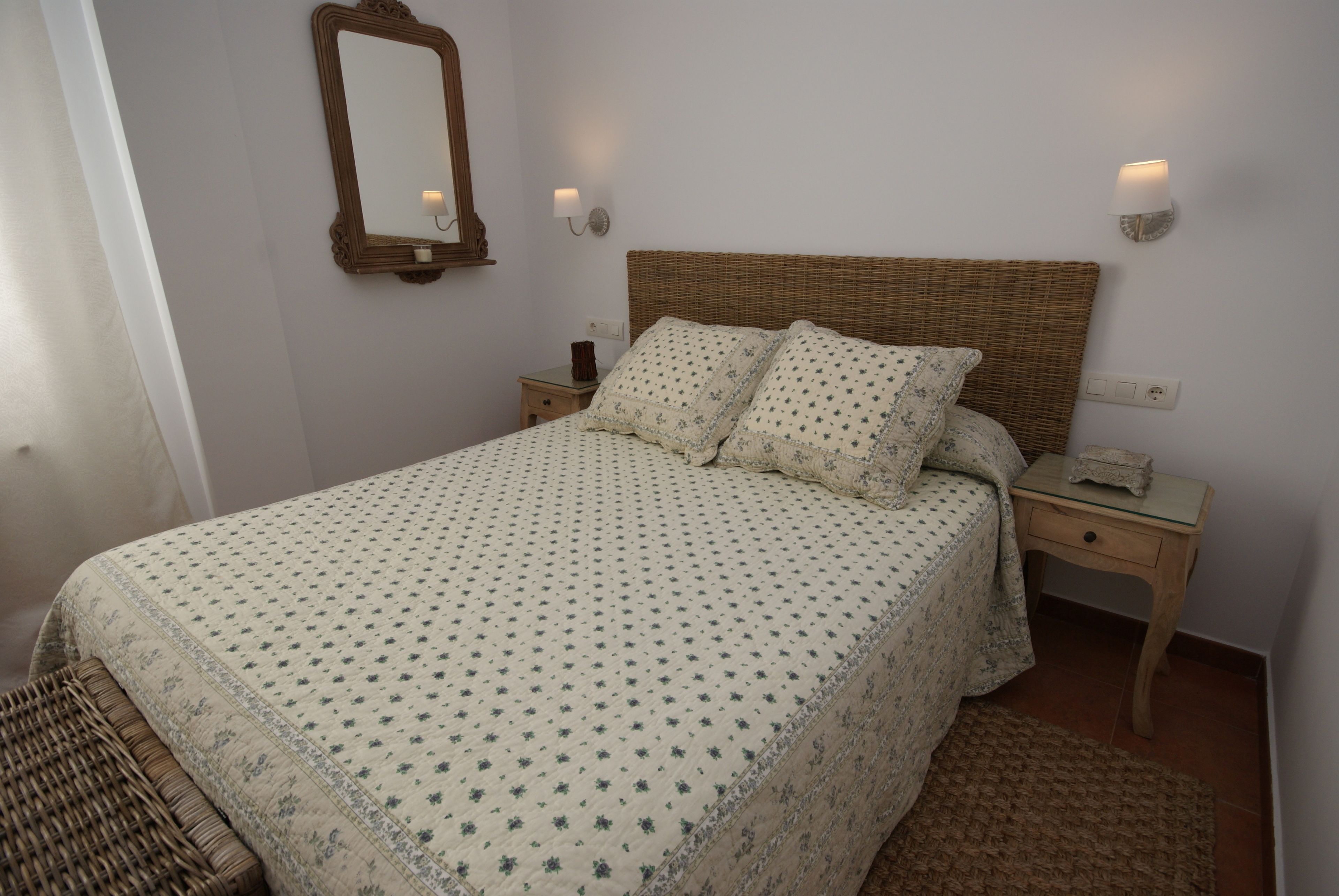 Un dormitorio con una cama grande, dos mesitas de noche, un tocador, un espejo y lámparas de pared.