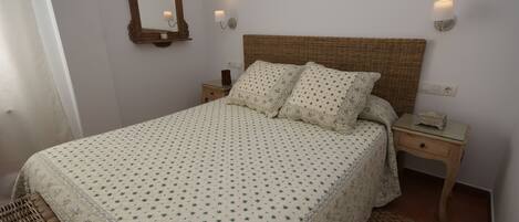 Un dormitorio con una cama grande, dos mesitas de noche, un tocador, un espejo y lámparas de pared.