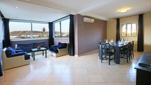 A spacious living area with a sofa set, a dining table, and a view of the cityscape through large windows. - Anezi Apartments (Agadir)