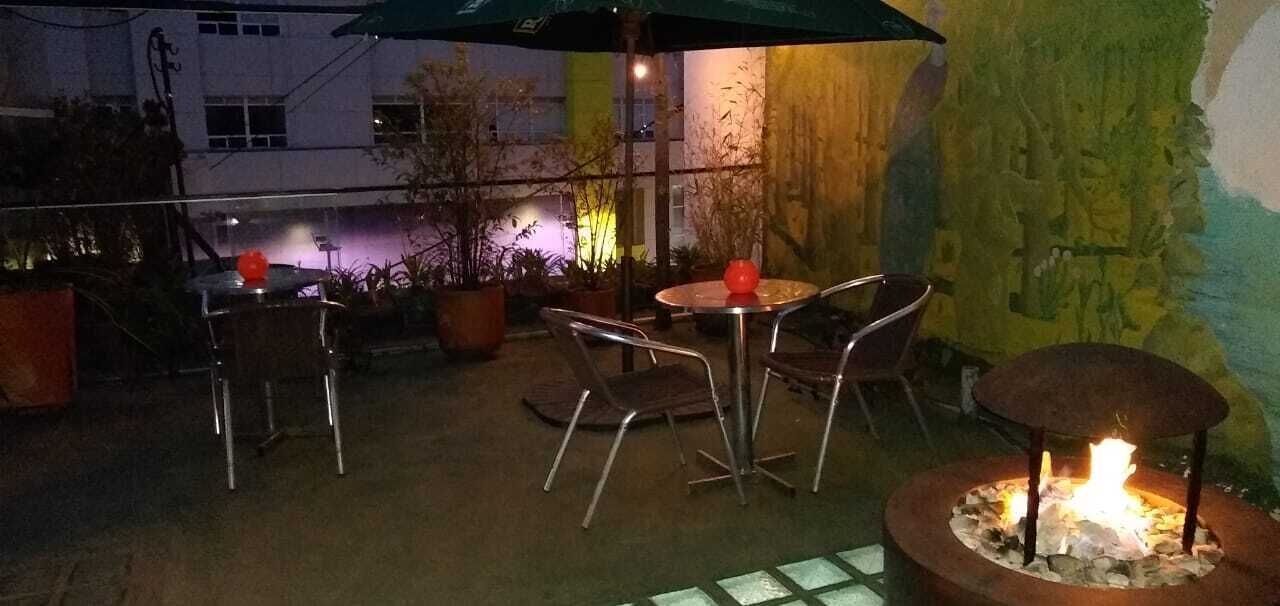 Un patio al aire libre con mesas, sillas, un hogar para fogata y plantas en macetas.