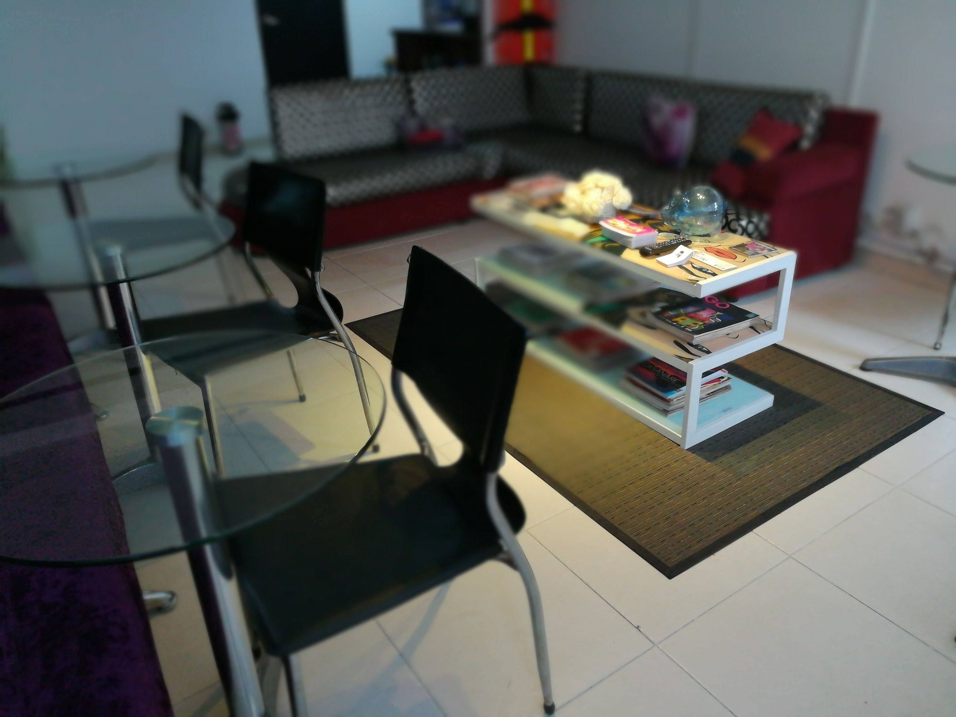 Una sala de estar moderna con una mesa de comedor de vidrio, sillas negras, una mesa de centro blanca con libros, un sofá rojo y un sofá gris.