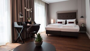 A modern hotel room with a bed, desk, chair, and a small table with a plant.