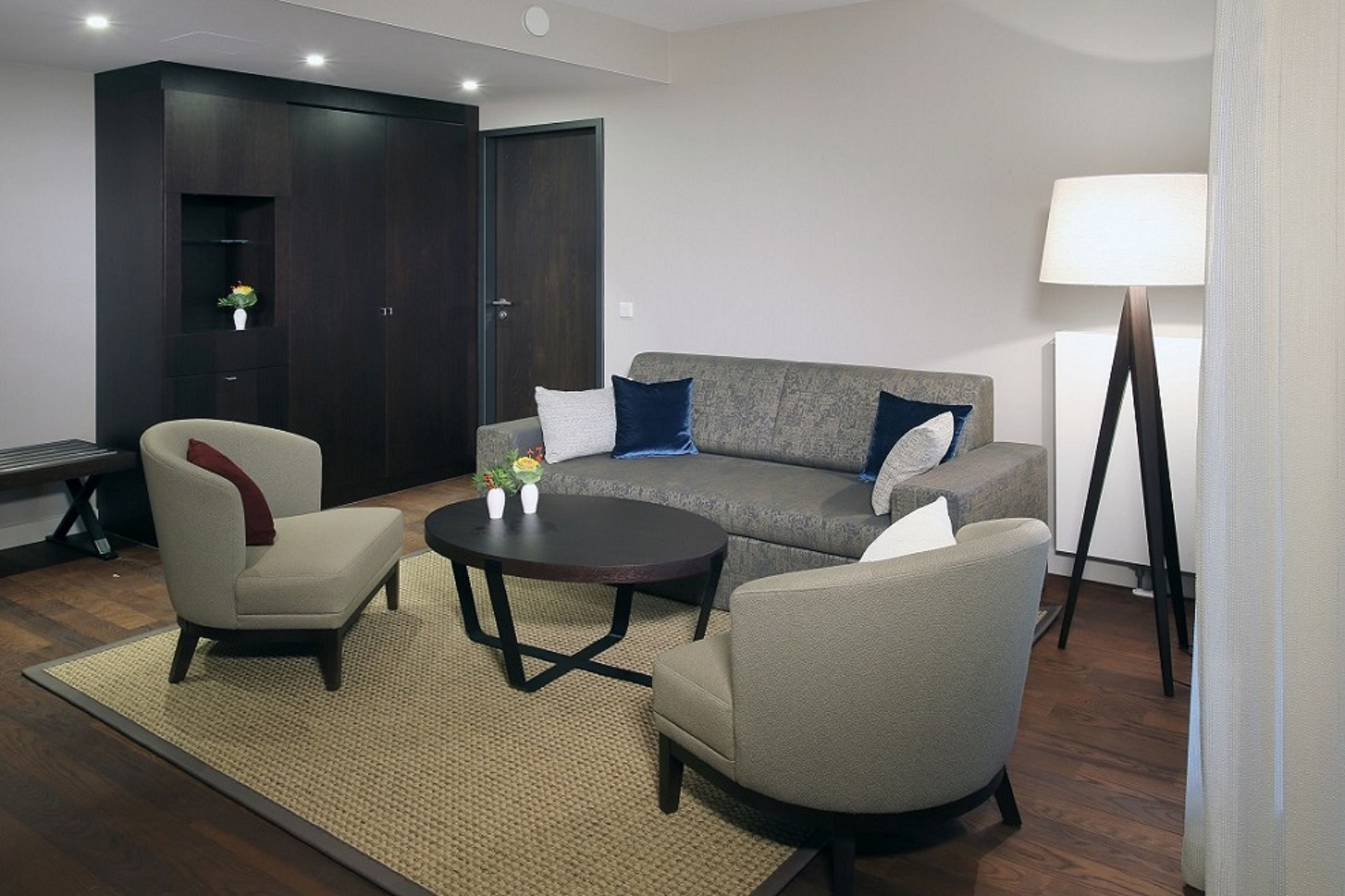 Ein modernes Wohnzimmer mit grauem Sofa, zwei Sesseln, einem Couchtisch und einer Lampe.