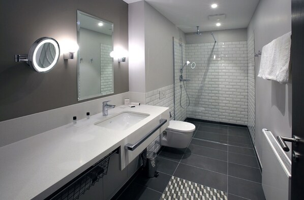 A modern bathroom with a dual sink vanity, a toilet, a shower, and a mirror with integrated lighting.