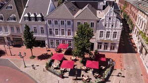 A historic European square with traditional architecture, outdoor seating, and a central fountain.