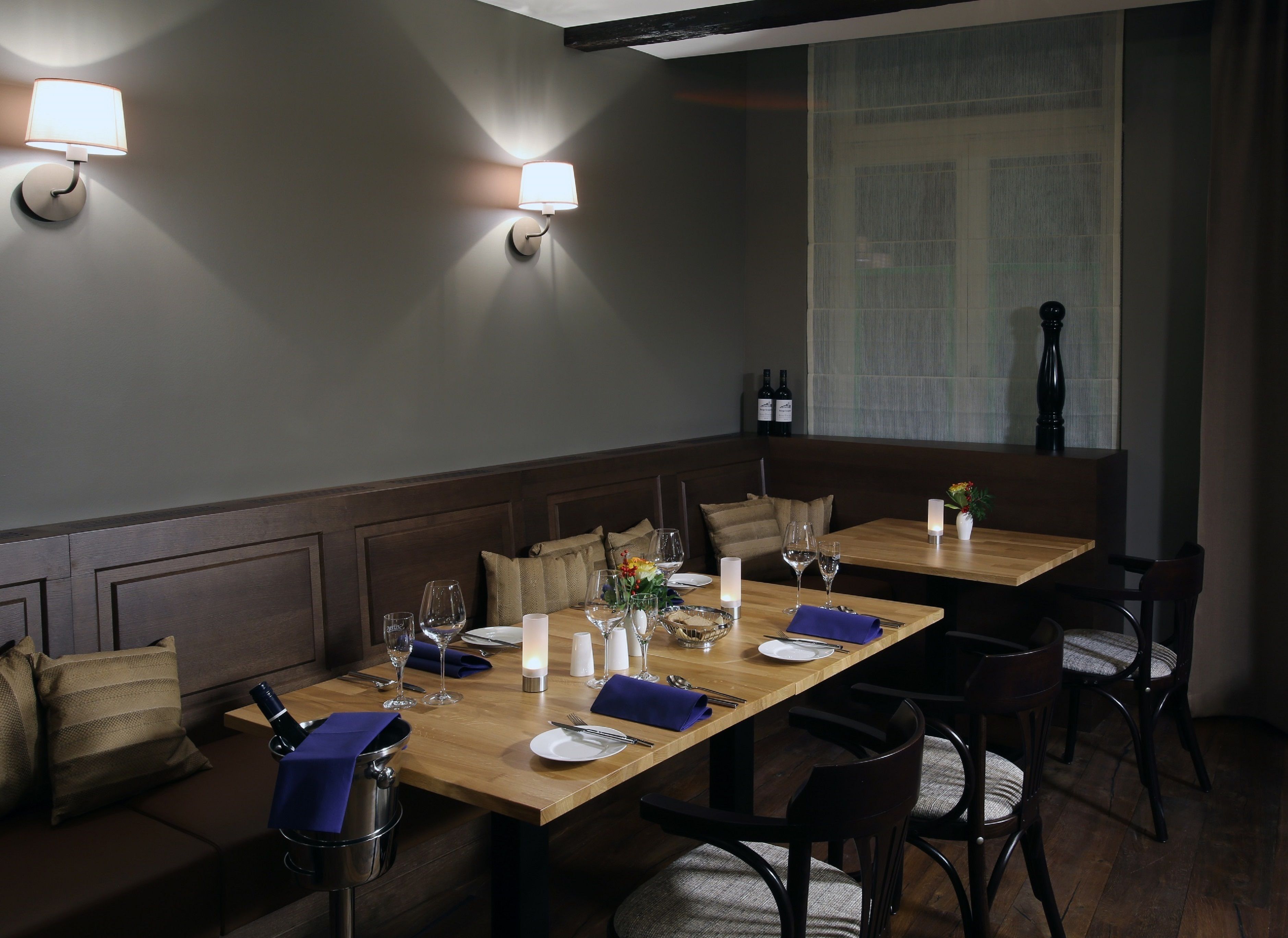 Un espace repas avec deux tables, chacune mise avec des assiettes, des verres et des couverts. Des lampes fixées au mur assurent l’éclairage.