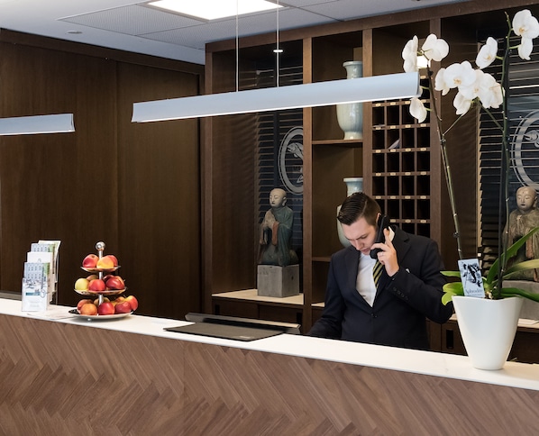 Un mostrador de recepción con una exhibición de frutas, un jarrón con orquídeas blancas y una estatua.