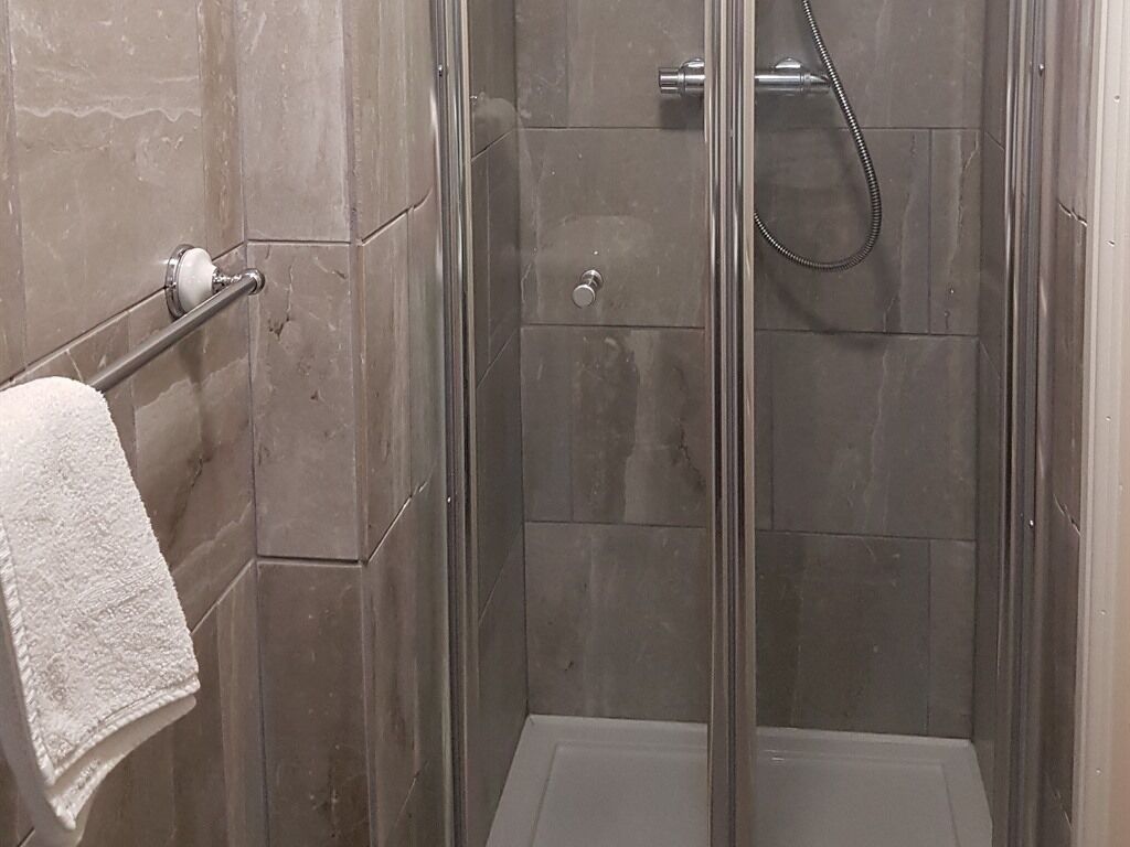 A shower with a glass door, a towel rack, and a shower control panel.