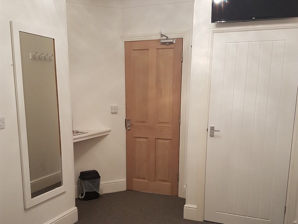 A hallway with a wooden door, a white door, and a mirror on the left wall.