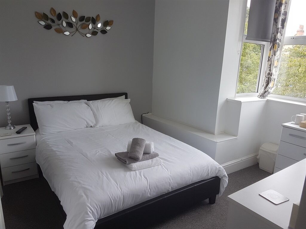 A neatly arranged bedroom with a bed, bedside tables, a lamp, and a window with a view.
