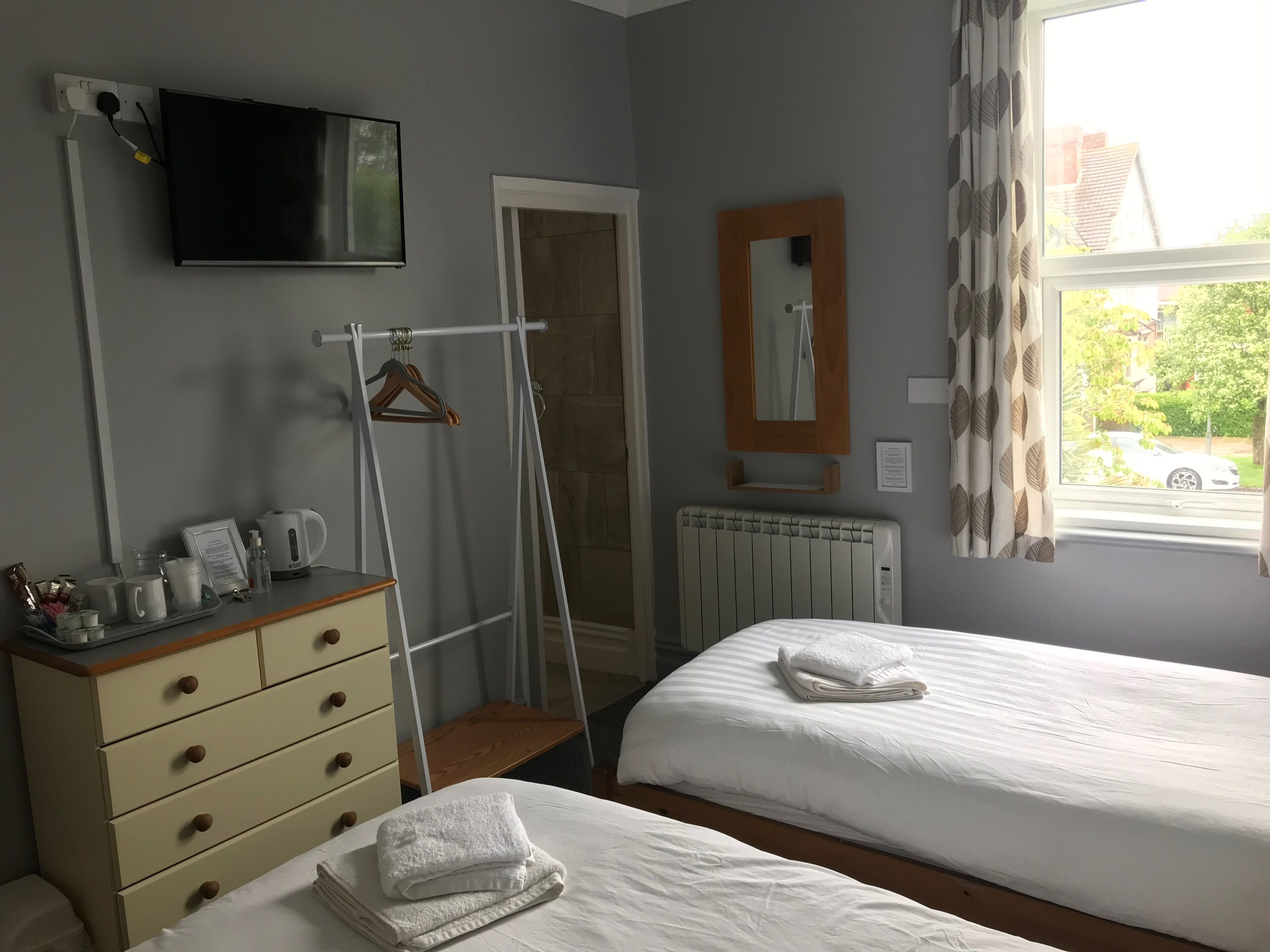 A hotel room with two beds, a TV, a radiator, a wooden dresser, and a window with curtains.