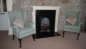 Two armchairs with patterned cushions, a fireplace with a stone wall backdrop, and a 'LAVATORY' sign on the left. - Sykes's House (Leyburn)