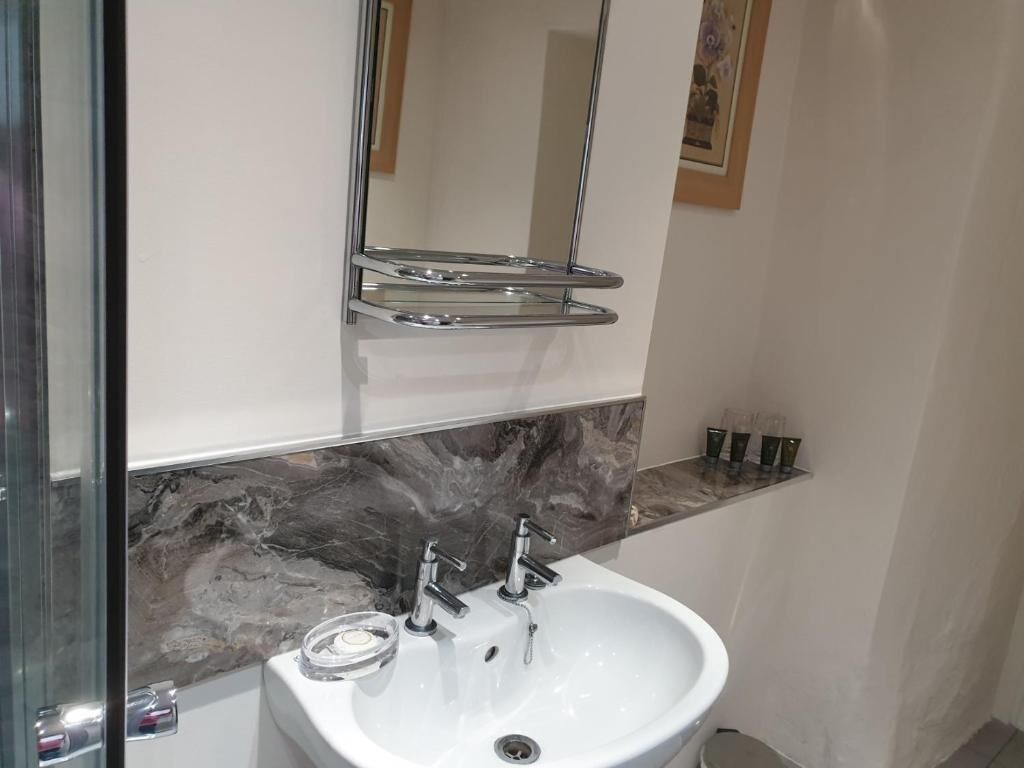 A bathroom with a white sink, two faucets, a mirror, and a marble backsplash.