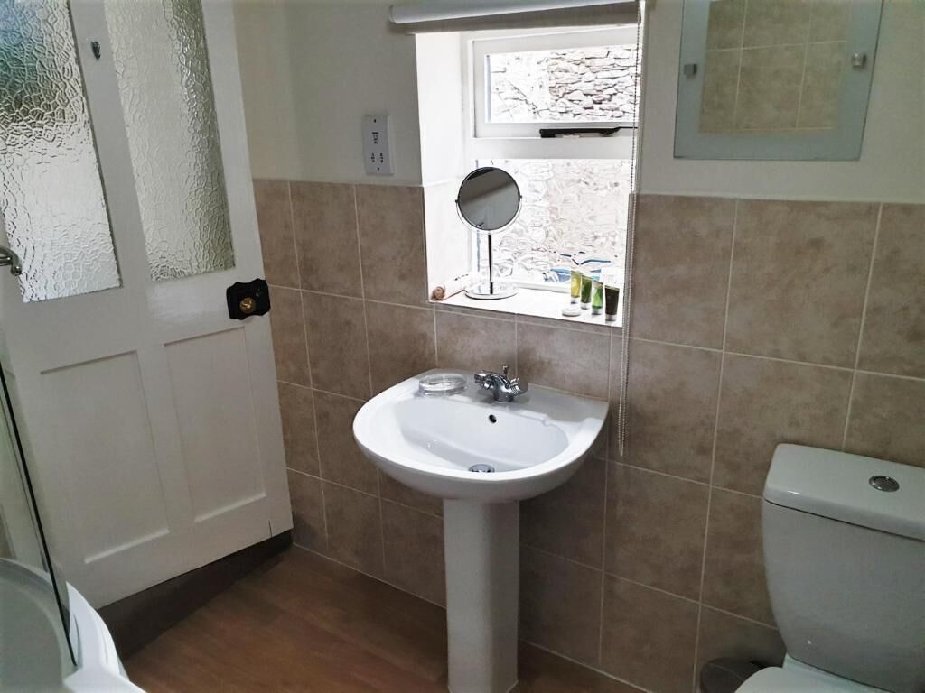 A bathroom with a white pedestal sink, a mirror, and a window with a view of the outside.