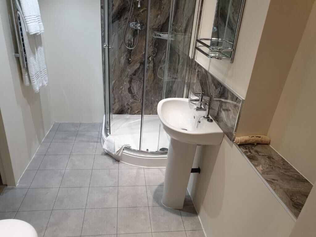 Une salle de bain dotée d’une douche à parois de verre, d’un lavabo sur colonne et d’un pare-baignoire en marbre.