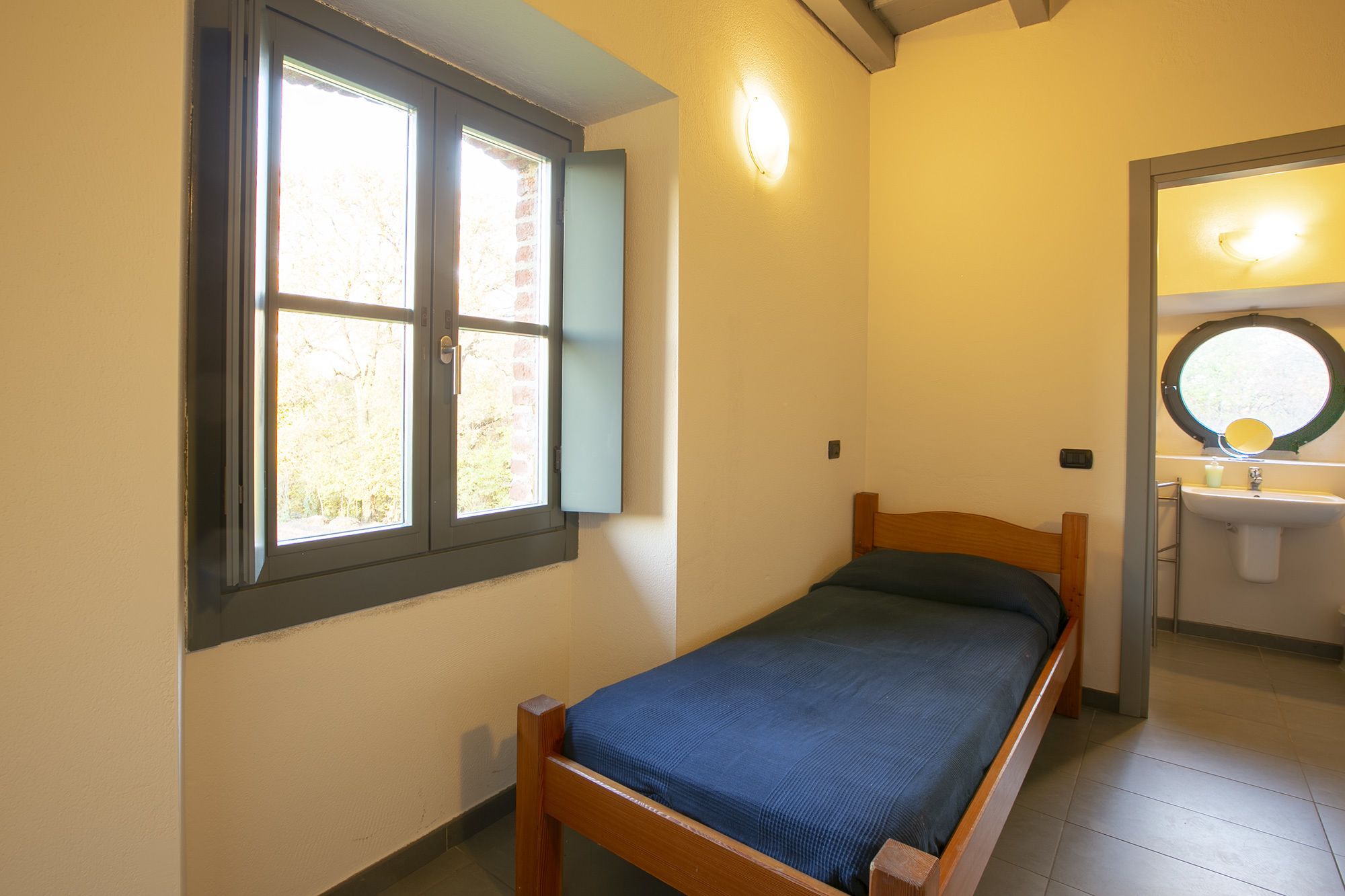A small, single-bed room with a window, a mirror, and a sink.