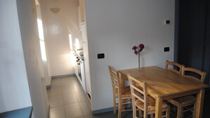 A dining area with a wooden table and chairs, a vase with flowers, and a kitchen in the background. - Ostello Costa Alta (Monza)
