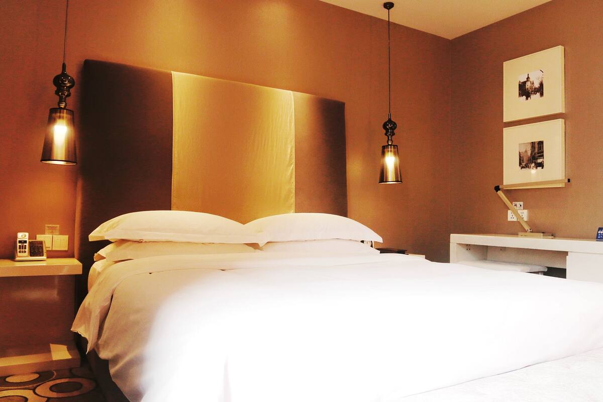 Habitación de hotel con una cama grande, dos lámparas de noche, una mesita de noche con teléfono y un estante en la pared con fotografías.