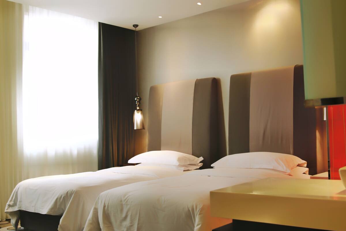 Habitación de hotel con dos camas, una mesita de noche y una ventana con cortinas.