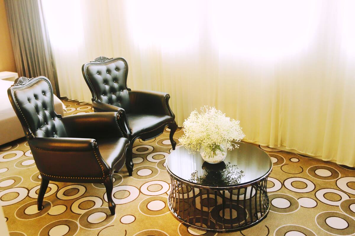 Una habitación con dos sillones de cuero negro, una mesa redonda con un florero de flores blancas y una alfombra estampada.
