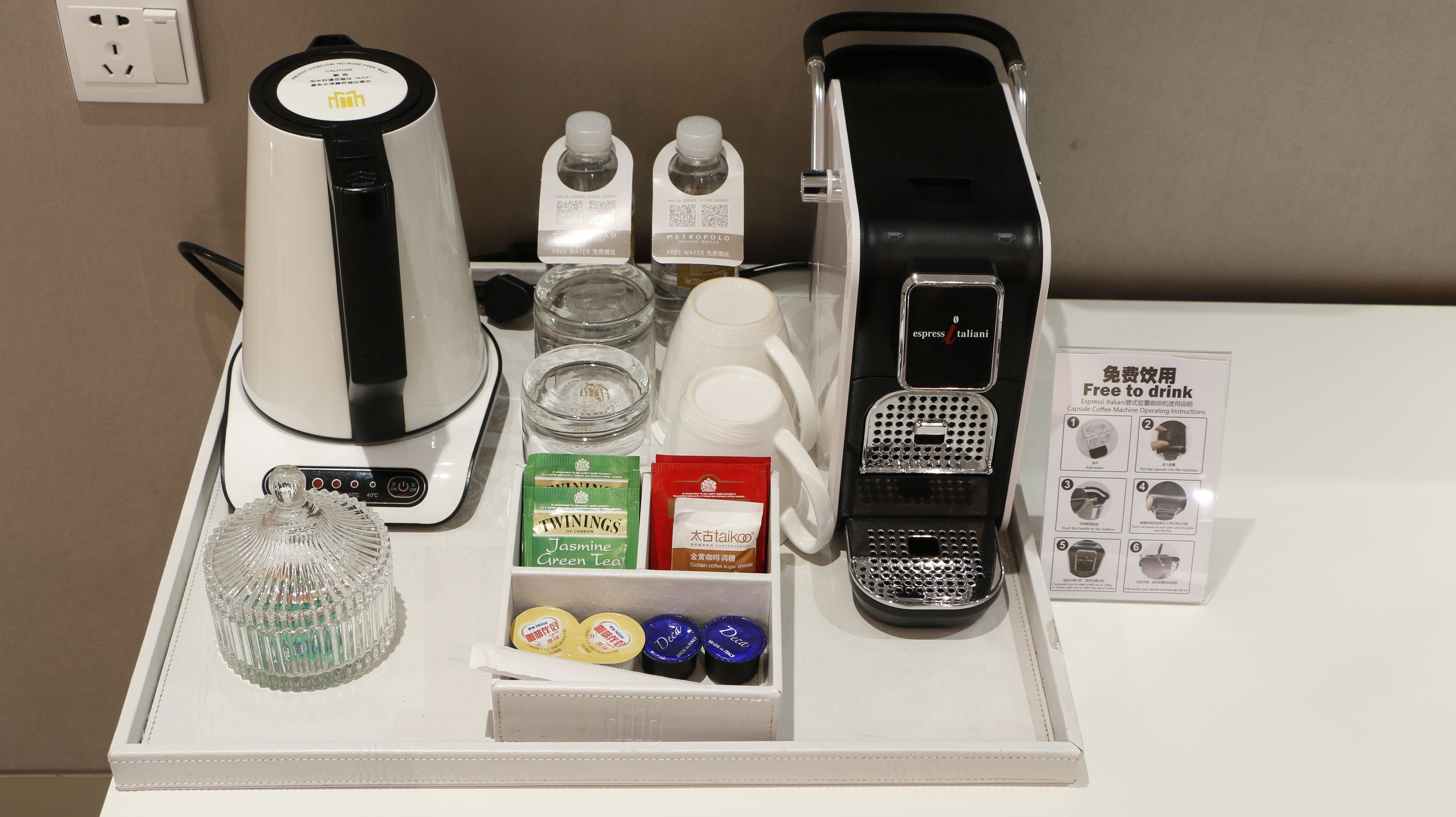 Una cafetera, un hervidor, un dispensador de cápsulas de café, una jarra de vidrio, una máquina de café y una caja de cápsulas sobre una mesa.