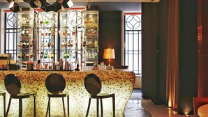 Zona de bar con mostrador de mosaicos, tres taburetes y una exhibición de botellas de licores.
