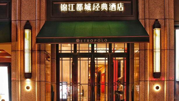 Entrada de hotel con fachada tradicional, toldo verde y señalización iluminada.