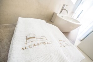 A white towel with "Castello" embroidered on it, placed on a bathroom floor next to a sink.