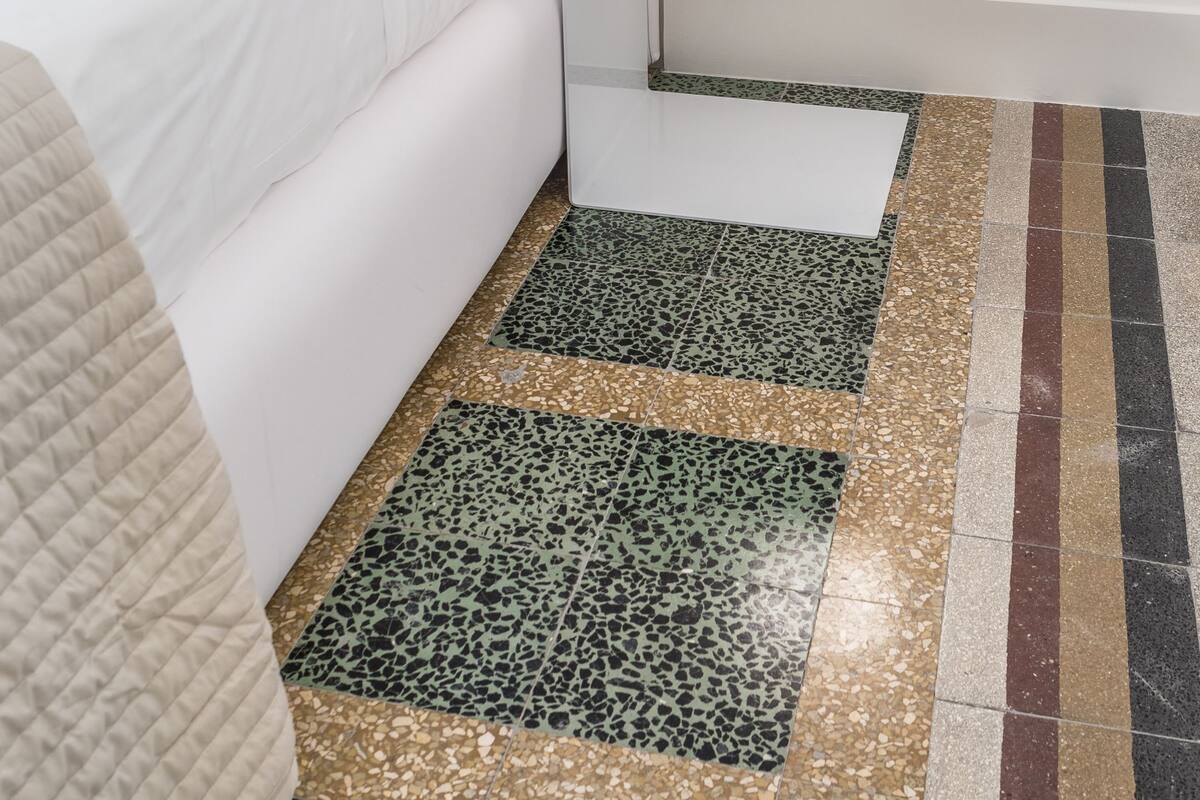 A bedroom with a bed, a bedside table with a lamp, and a patterned floor.