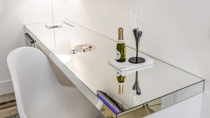 A modern room with a glass desk, a white chair, a TV mounted on the wall, a bottle of champagne, and a wine glass on the desk. - Home Boutique Luxury & Design (Reggio Calabria)