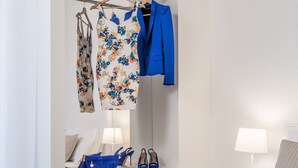 A hotel room with a bed, a bedside table with a lamp, a wardrobe with clothes, and a pair of shoes on the table. - Home Boutique Luxury & Design (Reggio Calabria)