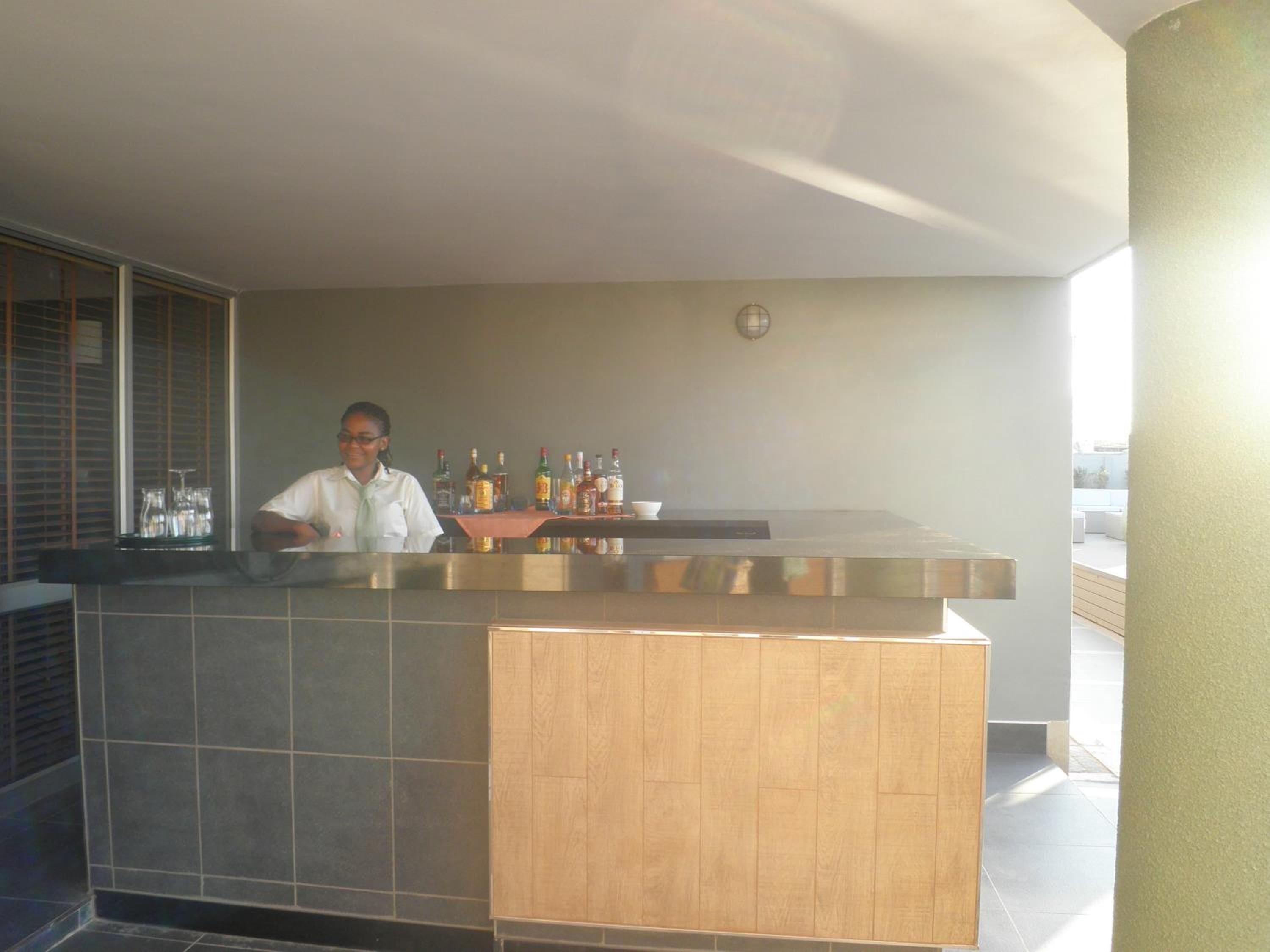 A bar area with a bartender, a counter with various bottles, and a view of the outdoors.