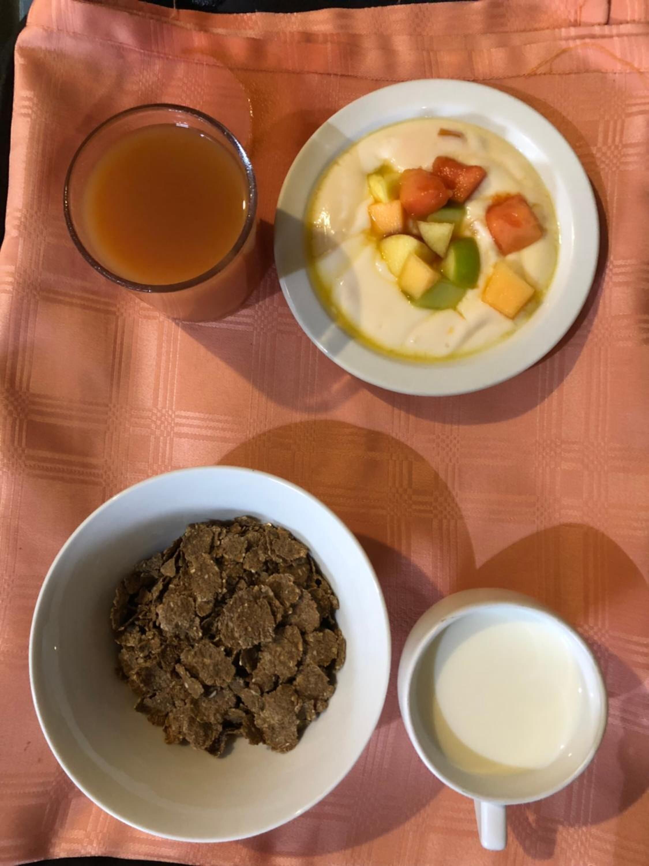 A meal consisting of a bowl of soup with vegetables, a glass of tea, a bowl of cereal, and a mug of milk on a table.