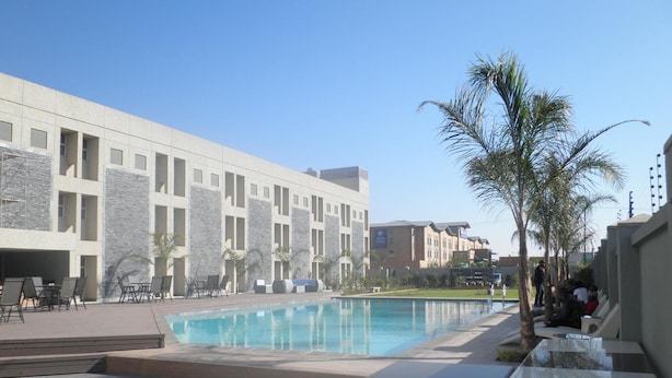 Un área de piscina con sillas de descanso y un edificio moderno con detalles de piedra.