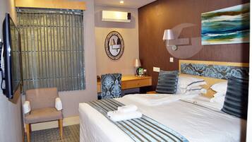 A hotel room with a bed, a chair, a desk, and a painting on the wall.