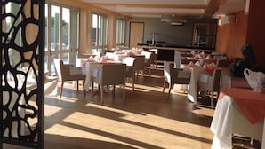 Un comedor espacioso con varias mesas y sillas, ventanas amplias que permiten la entrada de luz natural, y una zona de cocina al fondo.