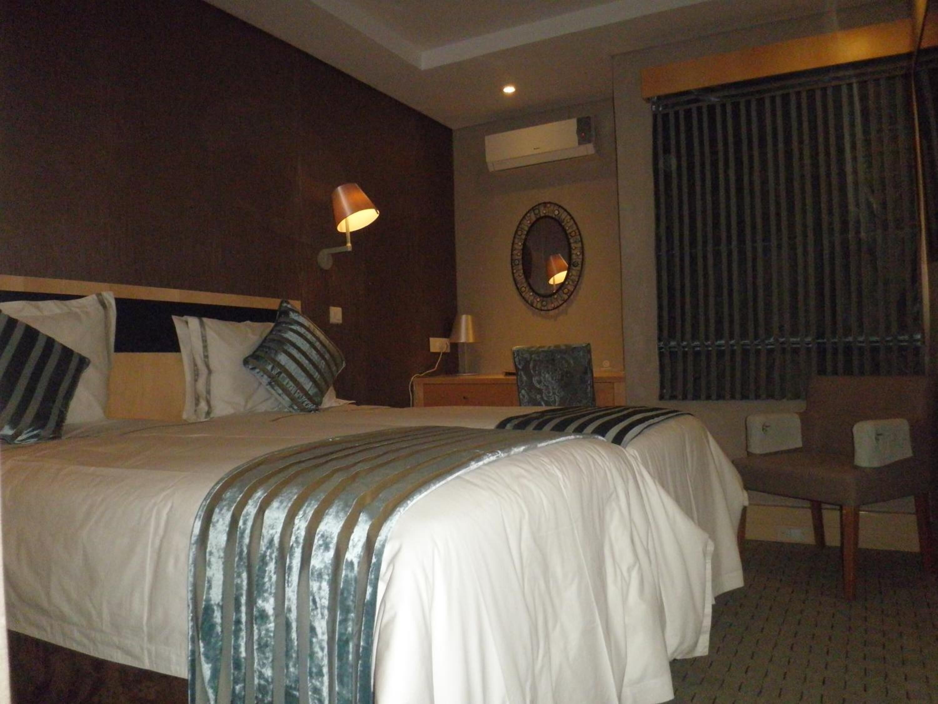 A hotel room with two beds, a chair, a desk, a mirror, and a window with curtains.