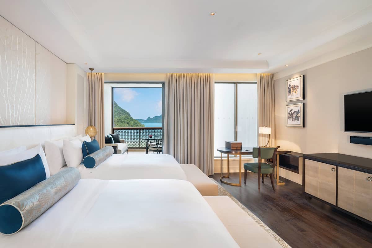 Une chambre d’hôtel avec deux lits, un bureau, une chaise, une télévision et un balcon avec vue.