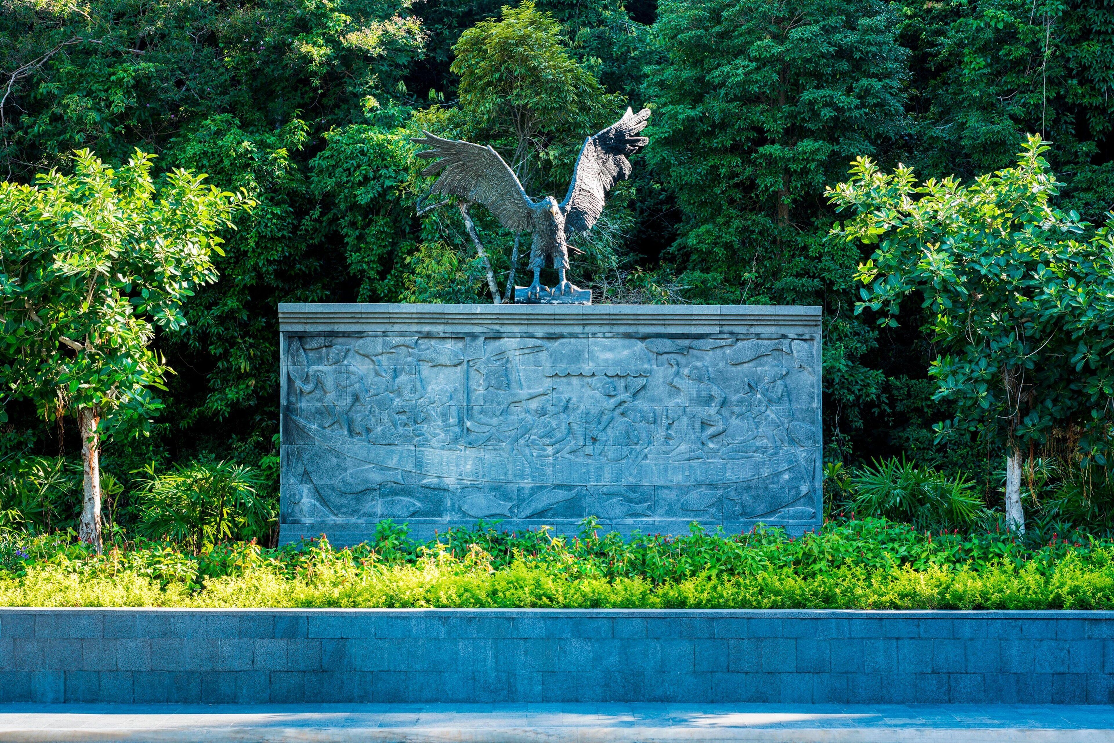 A sculpture of a bird on a stone pedestal surrounded by lush greenery.