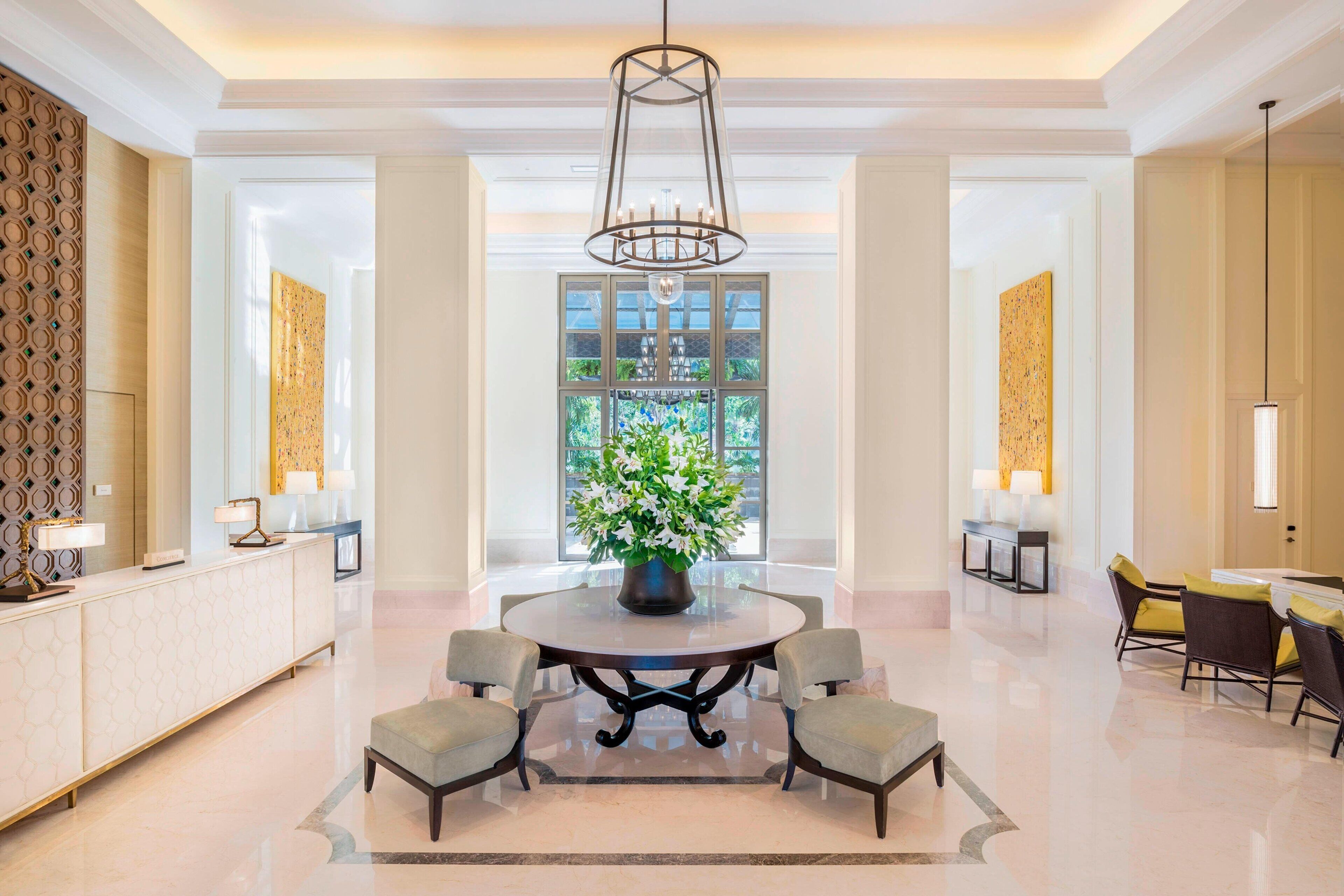 A spacious lobby with a round table, four chairs, a central flower arrangement, and a chandelier.