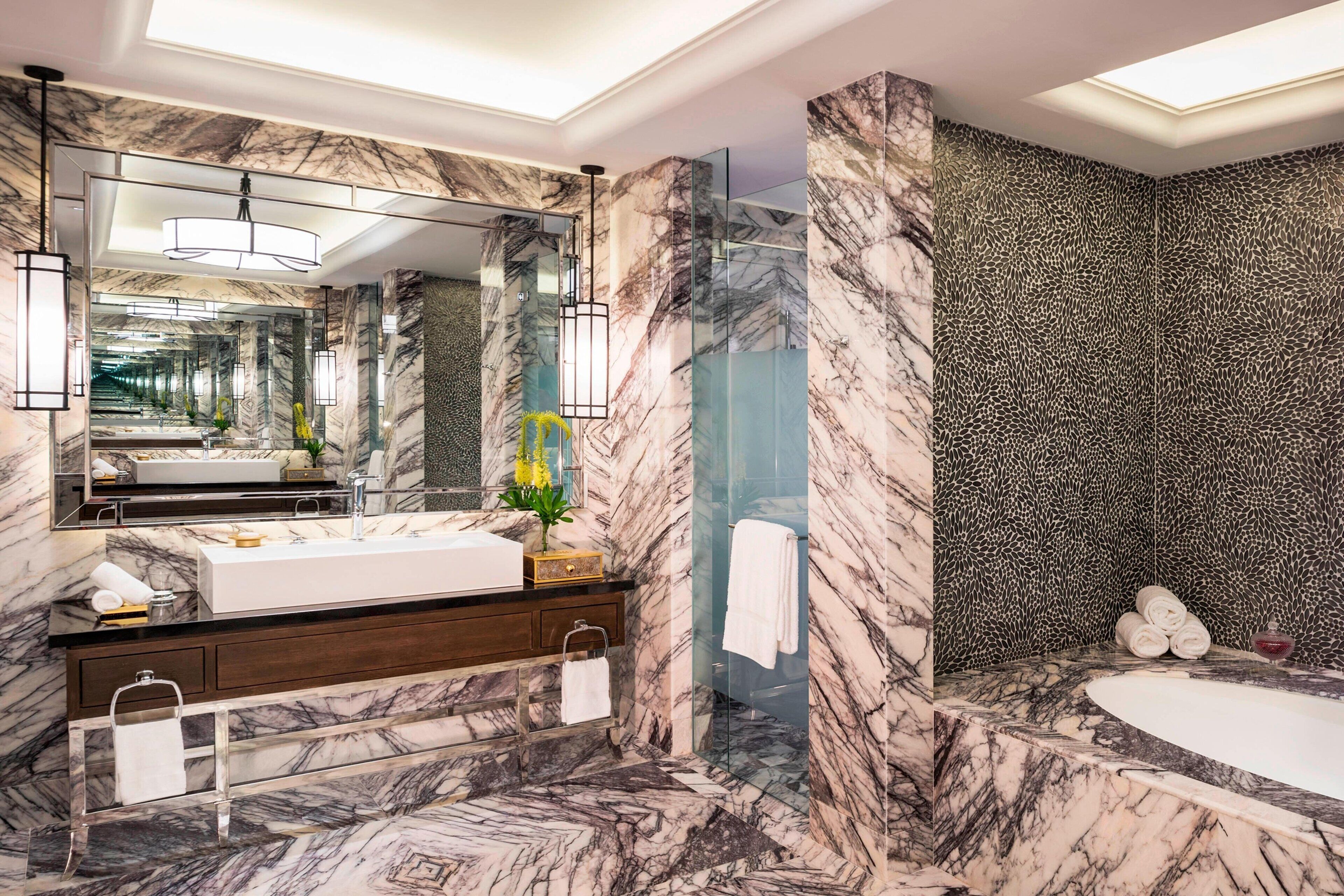 A luxurious bathroom with a marble vanity, a large mirror, a glass-enclosed shower, and a bathtub.