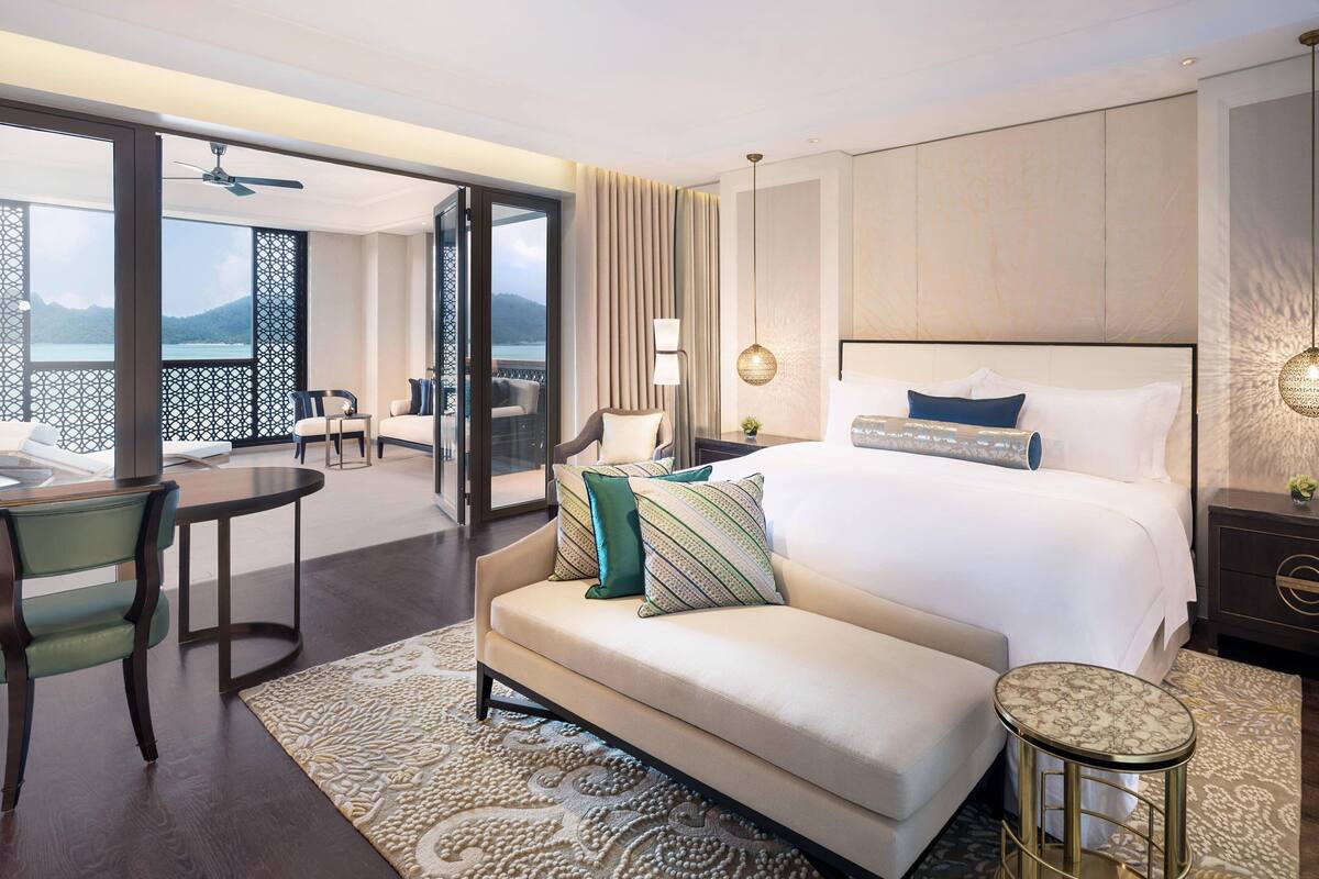 Une chambre d’hôtel avec un grand lit, un canapé, une table à manger et un balcon offrant une vue sur les montagnes.