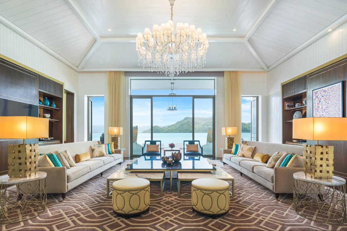 Un vaste salon doté d’une grande fenêtre donnant sur la mer, d’un lustre et d’un aménagement intérieur moderne.