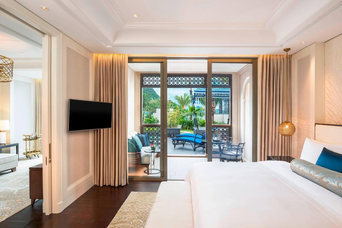 Une chambre d’hôtel dotée d’un grand lit, d’une télévision à écran plat, d’un balcon avec coin salon extérieur et offrant une vue sur la verdure.